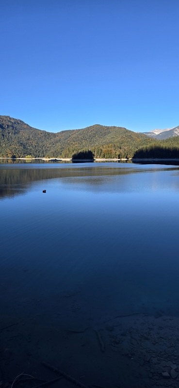 Blick über den Eibsee mit spiegelglattem Wasser und Bergkulisse am Morgen unserer Anreise nach Italien.