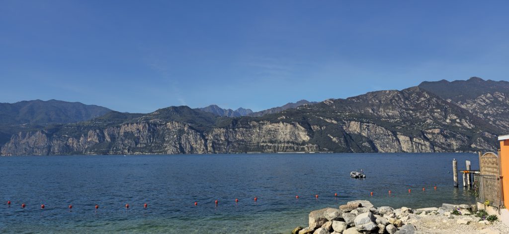Gardasee bei Malcesine im Oktober mit Berglandschaft, blauem Himmel und kristallklarem Wasser.